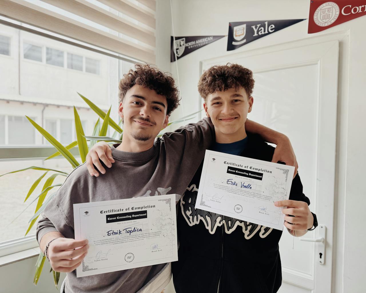 digital Two young adults proudly display their graduation certificates inside a classroom.