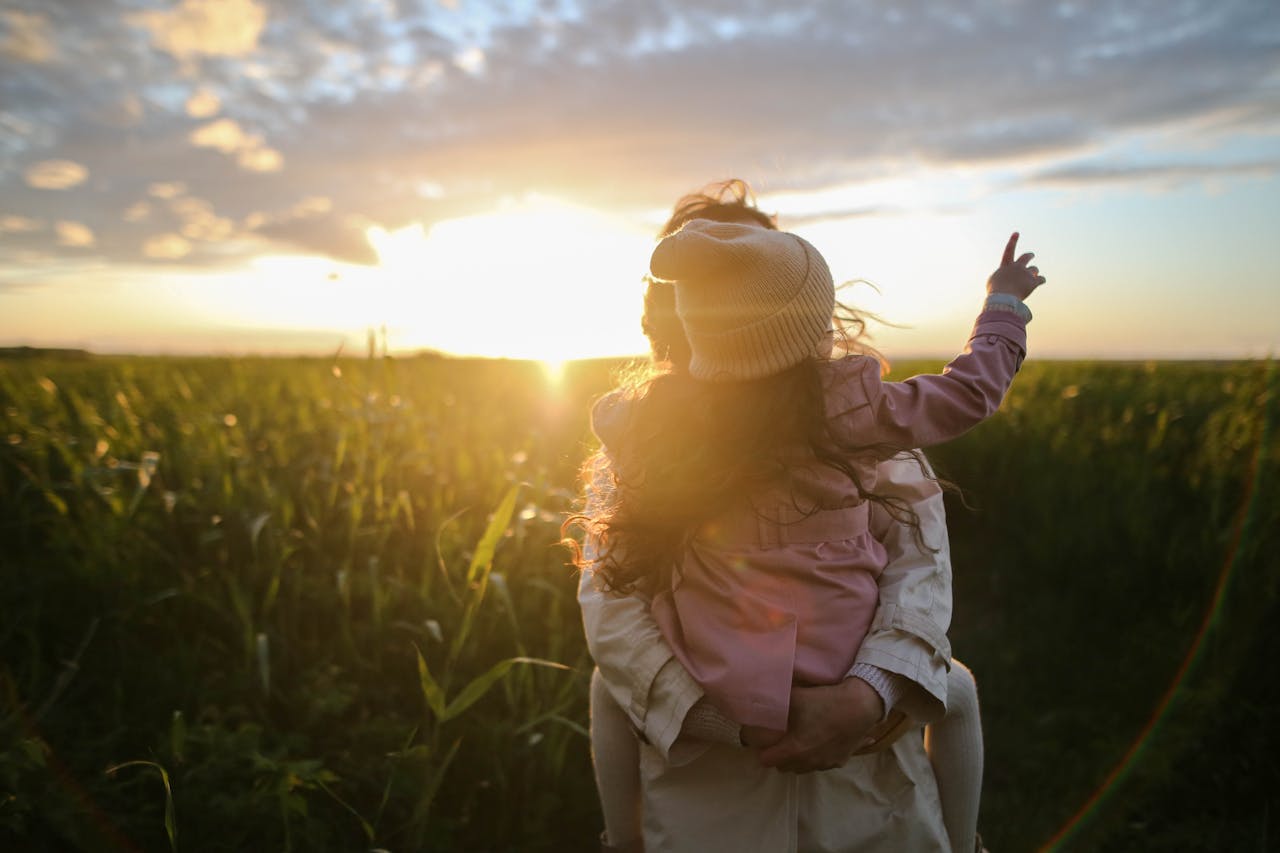 brand-01 A mother and daughter embrace and point at the sunset in a grassy field.