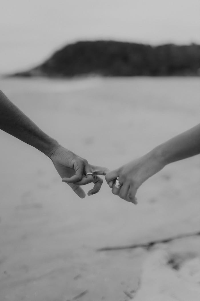 creative Black and white photo of two people holding hands on a serene beach.